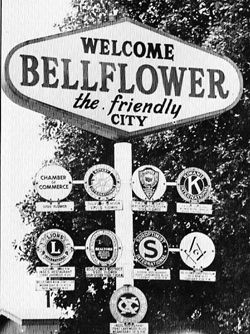 A large sign that reads Welcome - Bellflower - the friendly city - stands above smaller signs for local civic organizations in Bellflower, CA